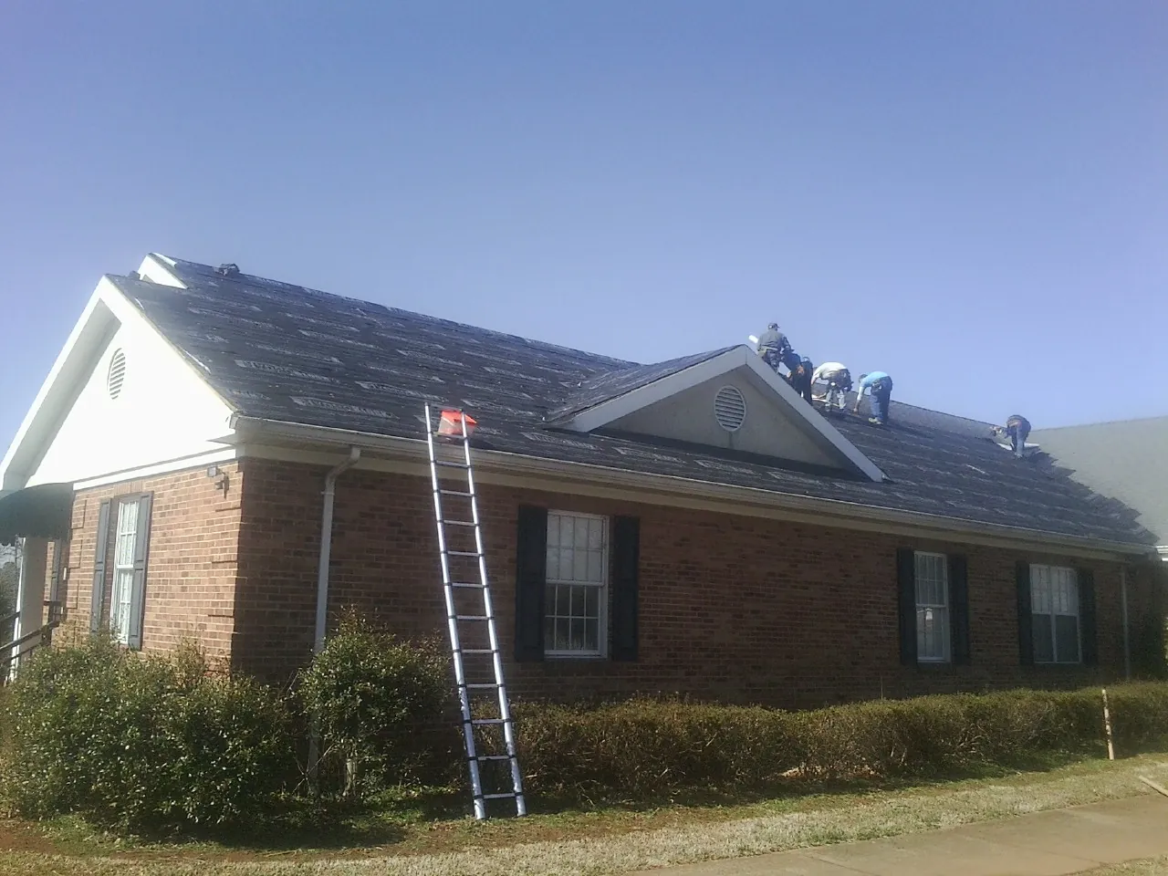 Crew tearing shingles off a brick ranch roof with a ladder set — Emergency Roof Repair work by our crew in Onondaga