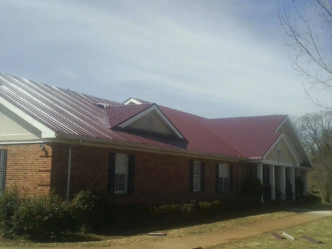 Red metal roof with gabled entries on a long brick building, from a Hail Damage Roof Repair job in Onondaga