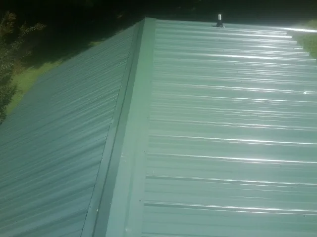 New green metal panels meeting at the ridge of a roof — Flat Roof Repair work by our crew in Onondaga
