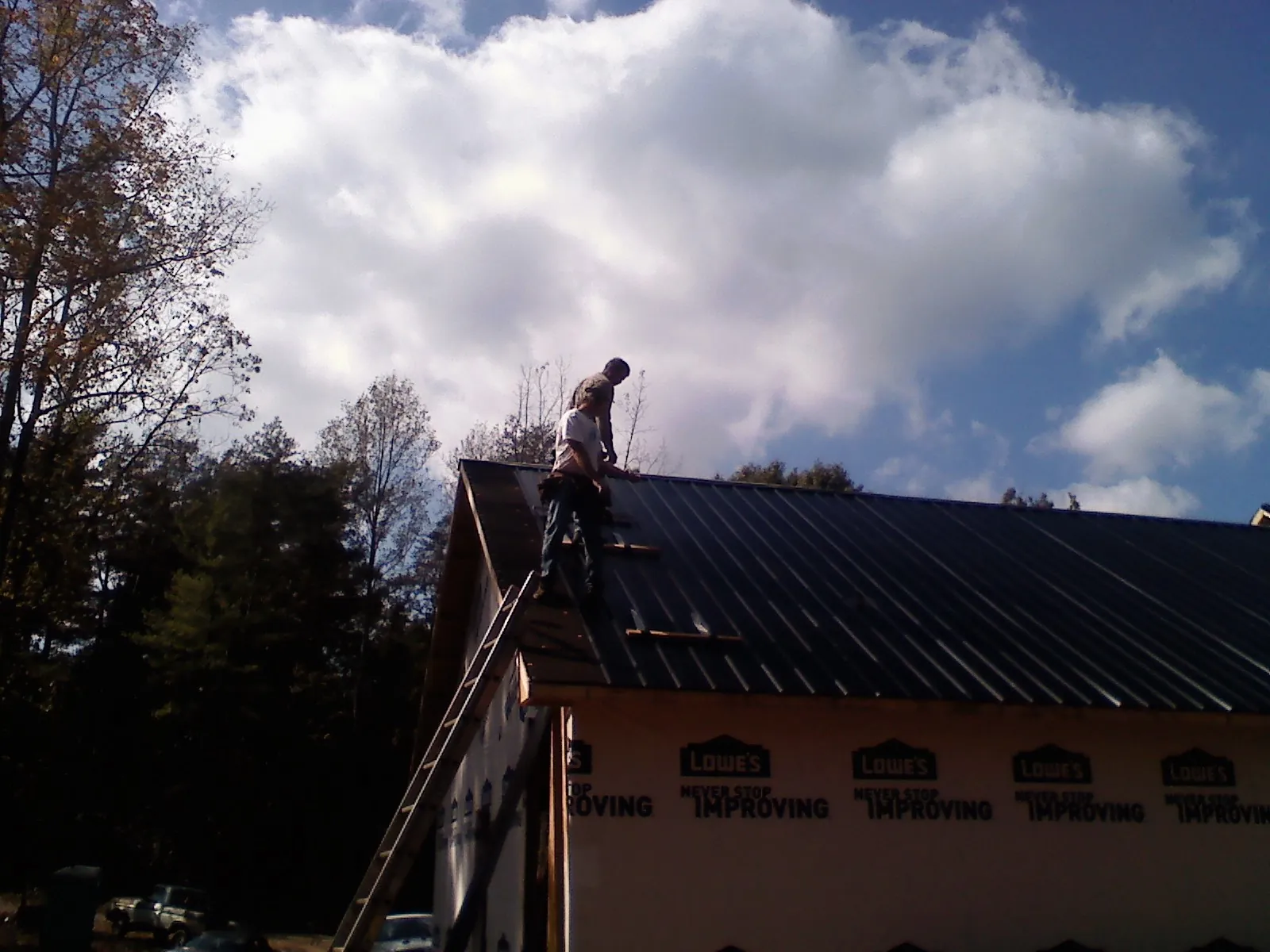 Roofer fastening dark metal panels high against a cloudy sky, from a Roof Inspection job in Onondaga