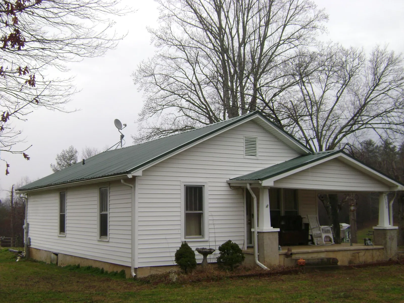 Green metal roof on a white bungalow with a side porch in Onondaga