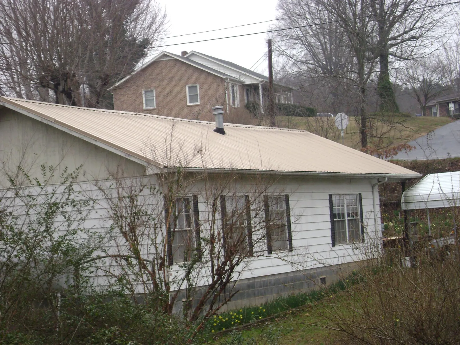 Tan metal roof on a white sided house set into a hillside — Commercial Roofing by Roofing Brothers in Onondaga
