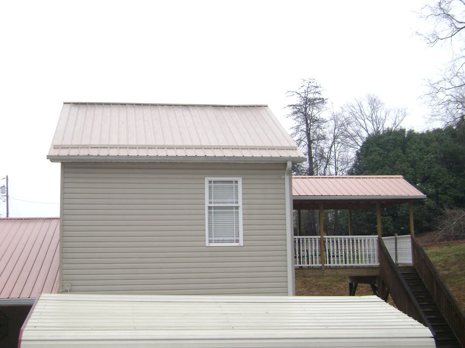 Tan metal roofs on a two story addition and attached porch, from a Roof Replacement job in Onondaga